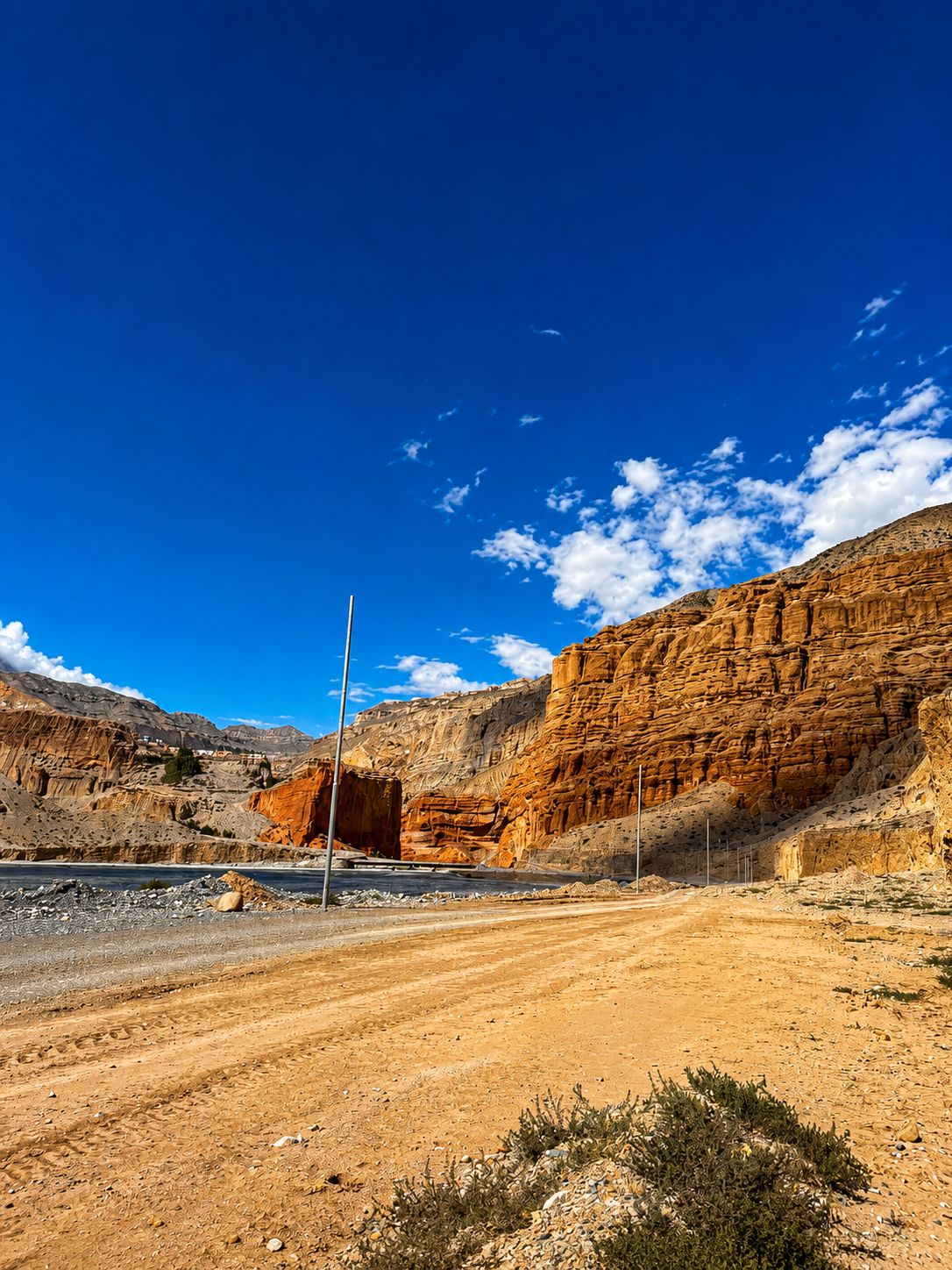Scenic dirt road winding through the dramatic desert cliffs and rock formations of Upper Mustang, Nepal beneath a clear blue Himalayan sky.