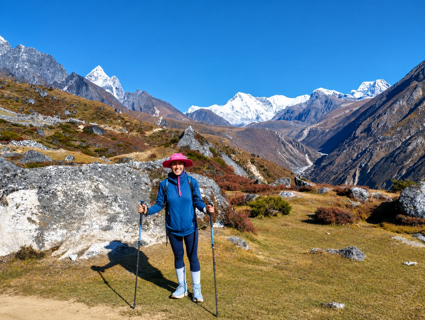 Trekker posing with trekking poles on the Everest Base Camp trail with snow-covered Himalayan mountains in the background.