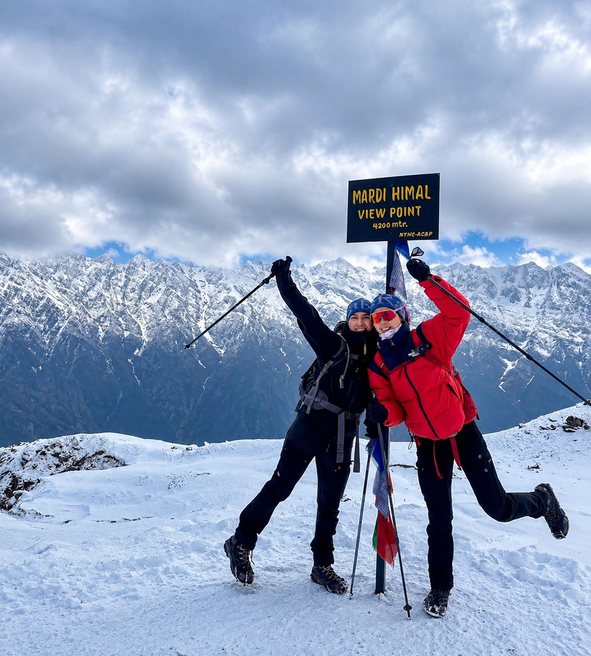 Trekkers posing at the Mardi Himal View Point sign surrounded by snow-covered Himalayan peaks in Nepal.